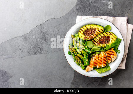 Gesund gegrilltes Huhn, gegrilltes Avocado und Spargelsalat mit Bettwäsche Samen. Ausgewogenes Mittagessen in der Schüssel. Grauer schiefer Hintergrund. Ansicht von oben. Stockfoto