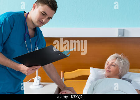 Junge männliche Arzt in Uniform mit phonendoscope auf seinem Hals ist die Messung der Puls seiner weiblichen Patienten, die im Krankenhaus in der Hosp liegt Stockfoto