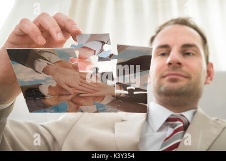 Low Angle View der Geschäftsmann Einfügen letzte Puzzleteil am Schreibtisch Stockfoto