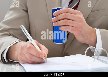 Nahaufnahme der Geschäftsmann mit Trinken kann und Schreiben auf Dokument Stockfoto