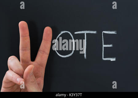 In der Nähe der Finger, V-Zeichen mit dem Wort Abstimmung am Schwarzen Brett Stockfoto