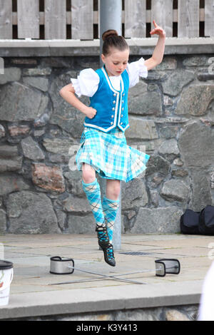 Ein junges Mädchen, das einen Schwerttanz mit Ullapool & District Junior Pipe Band in Ullapool, Schottland, aufführt Stockfoto