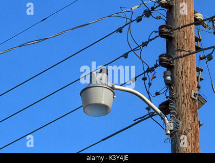 Einem unbeleuchteten Straßenlaterne auf einer hölzernen Pfosten mit Telefon Kabel zeichnet sich vor blauem Himmel. Stockfoto