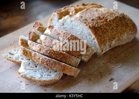 Frischen Laib Artisan Brot auf einem Holzbrett in Scheiben geschnitten wird. Stockfoto