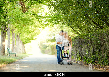 Mutter, Vater und Baby in einem Kinderwagen zu Fuß in den Park. Stockfoto