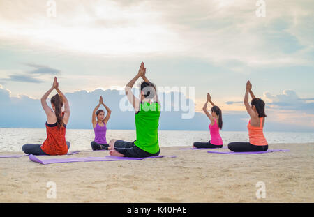 Yoga am Meer Strand im Sonnenuntergang am Abend, eine Gruppe von Leuten, die Namaste wirft mit Clam emotion am Strand entspannen, Meditation, Wellness und Gesunde b Stockfoto