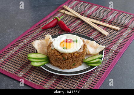Nasi Goreng gebratener Reis mit Krabben und Ei garniert mit frischen Gurkenscheiben und garnelencracker auf einem Schild auf einem Tuch. Asiatische Küche Stockfoto