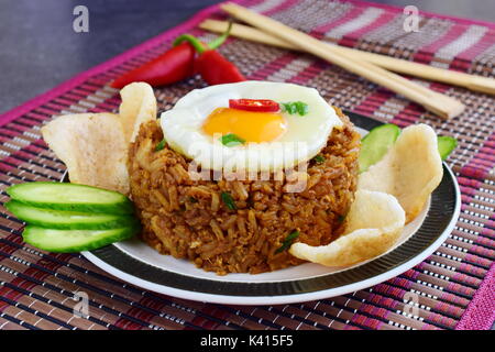 Nasi Goreng gebratener Reis mit Krabben und Ei garniert mit frischen Gurkenscheiben und garnelencracker auf einem Schild auf einem Tuch. Asiatische Küche Stockfoto