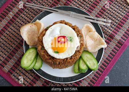 Nasi Goreng gebratener Reis mit Krabben und Ei garniert mit frischen Gurkenscheiben und garnelencracker auf einem Schild auf einem Tuch. Asiatische Küche. Stockfoto