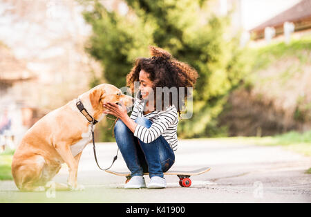 African American Girl im Freien auf Skateboard mit ihrem Hund. Stockfoto