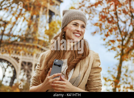 Herbst Kurzurlaube in Paris. lächelnde junge Touristen Frau in der Nähe von Eiffelturm mit Handy beiseite suchen Stockfoto