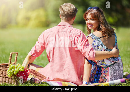 Ein Foto der Jungen, glückliches Paar entspannen auf dem Picknick. Das Mädchen wird von ihrem Freund umarmte und ist glücklich lächelnd. Stockfoto