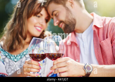 Ein Foto des jungen Paares Hals über Kopf verliebt. Sie feiern ihr Jubiläum in der frischen Luft und trinken Rotwein. Stockfoto