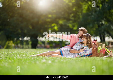 Ein Foto des jungen Paares Relaxen im Park und tranken Rotwein. Sie sind auf der Suche nach etwas. Stockfoto