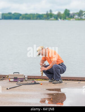 Man entfernt einen Haken von einem Fisch, den er vor der Freigabe einer Pier in Orillia Ontario Kanada gefangen. Stockfoto