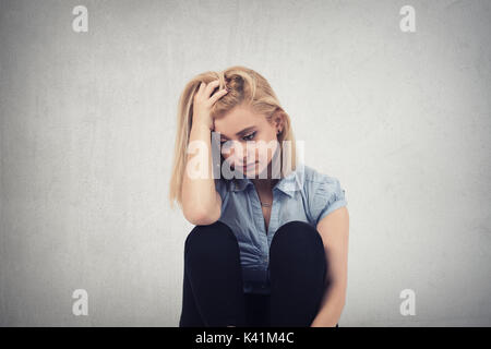 one sad woman sitting on the floor near a wall and holding her head in her hands Stockfoto