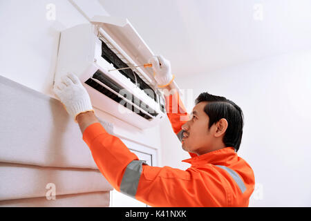 Jungen asiatischen männlichen Techniker Reparatur Klimaanlage mit Schraubendreher zu Hause Stockfoto