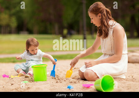 Glückliche Mutter und Baby Mädchen spielen in Sandbox Stockfoto