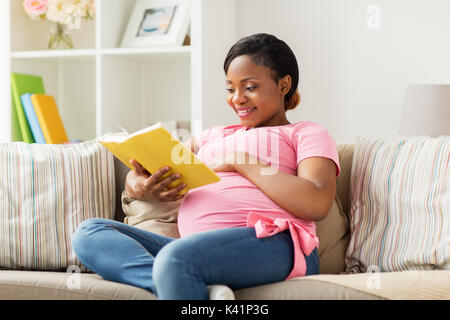 Glücklich schwanger afrikanische Frau mit Buch zu Hause Stockfoto