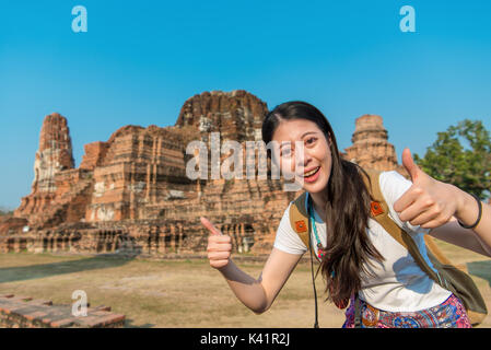 Schönheit lächelnd weibliche Touristen besuchen Sie Ayutthaya berühmten Wat Mahathat und "Daumen hoch" Geste der Aufnahme in Thailand reise. Stockfoto