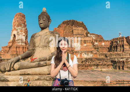 Lächelnden jungen Mädchen Schüler besuchen Sie Ayutthaya berühmten Wat Mahathat und Stellung vor Buddha, Beten Geste mit Gesicht zur Kamera in Thaila Stockfoto