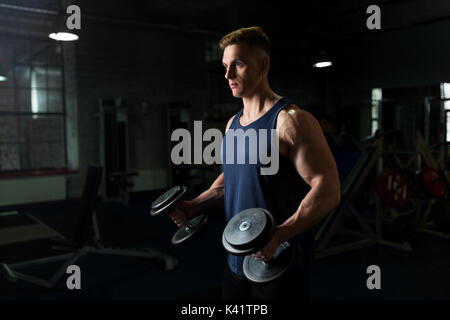 Junger Mann mit Hanteln trainieren im Fitnessraum Stockfoto