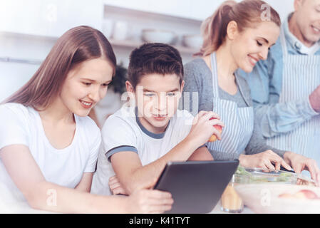 Charming kids Spielen auf digital Tablet während die Eltern kochen Stockfoto