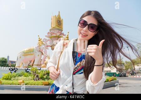 Lächelnd weibliche Reisende stand vor der berühmten Super Grand Palace Gebäude unter Bild und "Daumen hoch" Geste Gesicht Kamera auf Bangkok zu Stockfoto