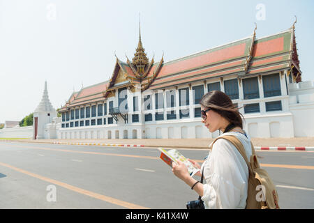 Lächelnd ziemlich touristische Frau liest Reiseführer stehen auf Grand Palace am Straßenrand suche Informationen Karte in Bangkok, Thailand reisen. Stockfoto