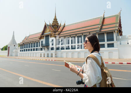 Schöne süsse weibliche Backpacker holding Reiseführer und Suchen nach Zielort in Bangkok, Thailand Reise mit dem berühmten Grand Palace. Stockfoto