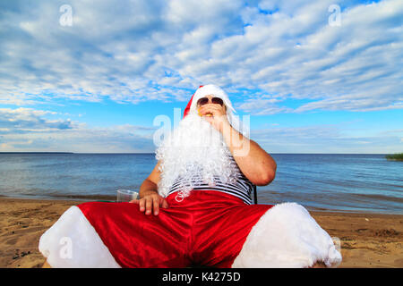 Santa Claus am Strand essen einen Hamburger. Das Konzept der ungesunden Ernährung. Stockfoto