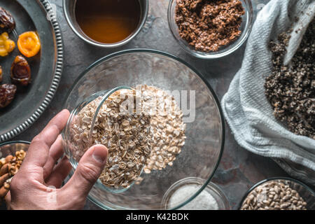 Hand mit einer Schüssel mit Hafer, Zutaten für das Müsli und Schüssel horizontal Stockfoto