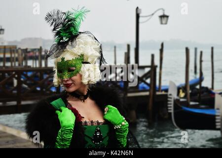 Eine Dame in einem wunderschönen grünen Kostüm während des Karnevals von Venedig mit Gondeln im Hintergrund. Stockfoto