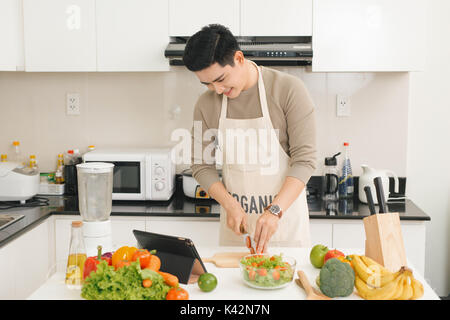 Asiatische schöner Mann suche Rezept auf Laptop in der Küche zu Hause. Stockfoto