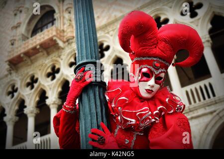 Eine Person, die in einem roten joker Kostüm an einen Laternenpfahl während einer Maskerade im Karneval von Venedig. Stockfoto