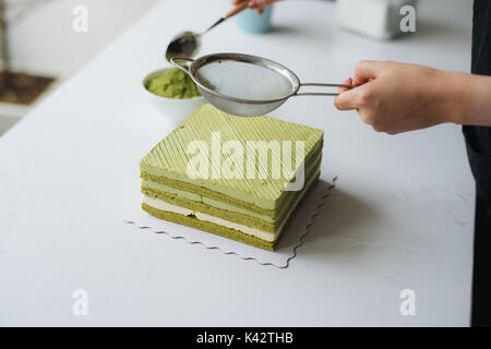 Gießen grüner Tee Pulver über leckeren Käsekuchen Stockfoto