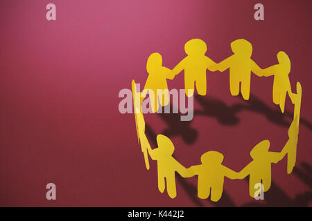 Gruppe von gelben kleine Person halten sich an den Händen gegen den roten Hintergrund Stockfoto