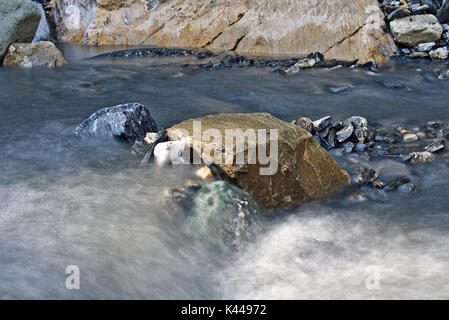 Felsbrocken in einem kleinen Gebirgsbach umgeben von sanften fließenden Wassers (Langzeitbelichtung) Stockfoto