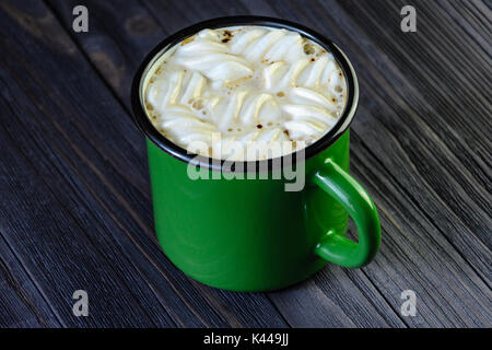 Heißes Getränk mit weißen Marshmallows in einem grünen Emaille Tasse auf einem schwarzen Holztisch Ansicht von oben. Dunklen Hintergrund. Stockfoto