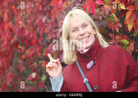 Glücklich lächelnde ältere Frau im Herbst Park über die roten Blätter Hintergrund Stockfoto