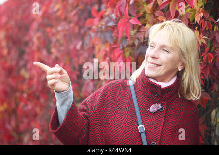 Glücklich lächelnde ältere Frau im Herbst Park über die roten Blätter Hintergrund Stockfoto