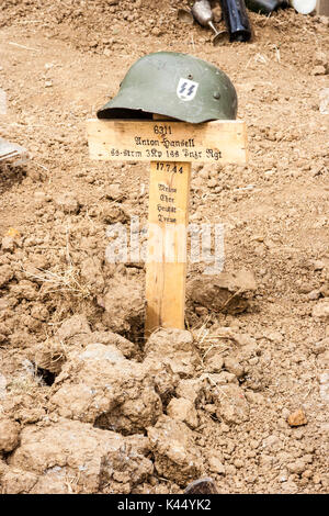 Zweiten Weltkrieg Re-enactment, lebendige Geschichte. Bis Grab der Waffen-SS Soldaten, Helm auf hölzernen Kreuz geklebt mit Inschrift auf, frisch gegraben Erde. Stockfoto