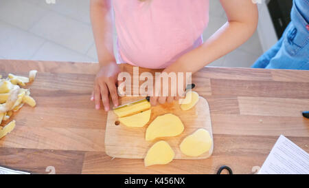 Kind schneidet Kartoffeln in Stücke mit einem scharfen Messer Stockfoto