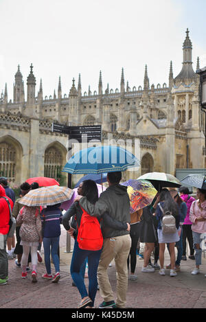 Gruppen von ausländischen Touristen mit einem Reiseleiter außerhalb Kings College in Cambridge mit ihren bunten Schirmen versammeln Stockfoto