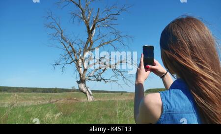 Mädchen nimmt Bilder von einem Baum. Touristische holding Telefon Mobiltelefon unter Foto trockenen Baum lifestyle Natur Stockfoto
