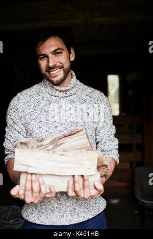 Scheune, Mann mit Strickpullover mit Brennholz, heiter, halb-Porträt, Stockfoto