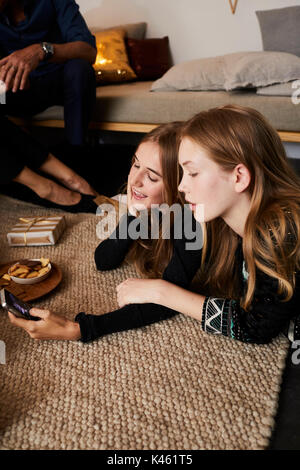 Weihnachten, zwei Mädchen liegen mit Handy auf dem Teppich, Stockfoto