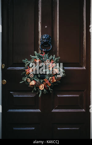 Weihnachten Kranz auf eine dunkle braune Holztür mit Türklopfer aus Metall Stockfoto