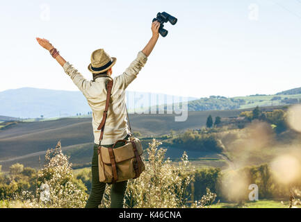 Entdecken Sie magische Ausblicke auf die Toskana. Von hinten Frau Wanderer mit Tasche wandern in der Toskana mit dem Fernglas gesehen Freude Stockfoto