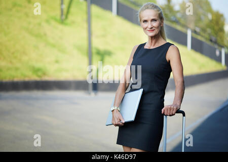 Gesicht portrait von zuversichtlich Geschäftsfrau holding Koffer Griff und Laptop. Stockfoto